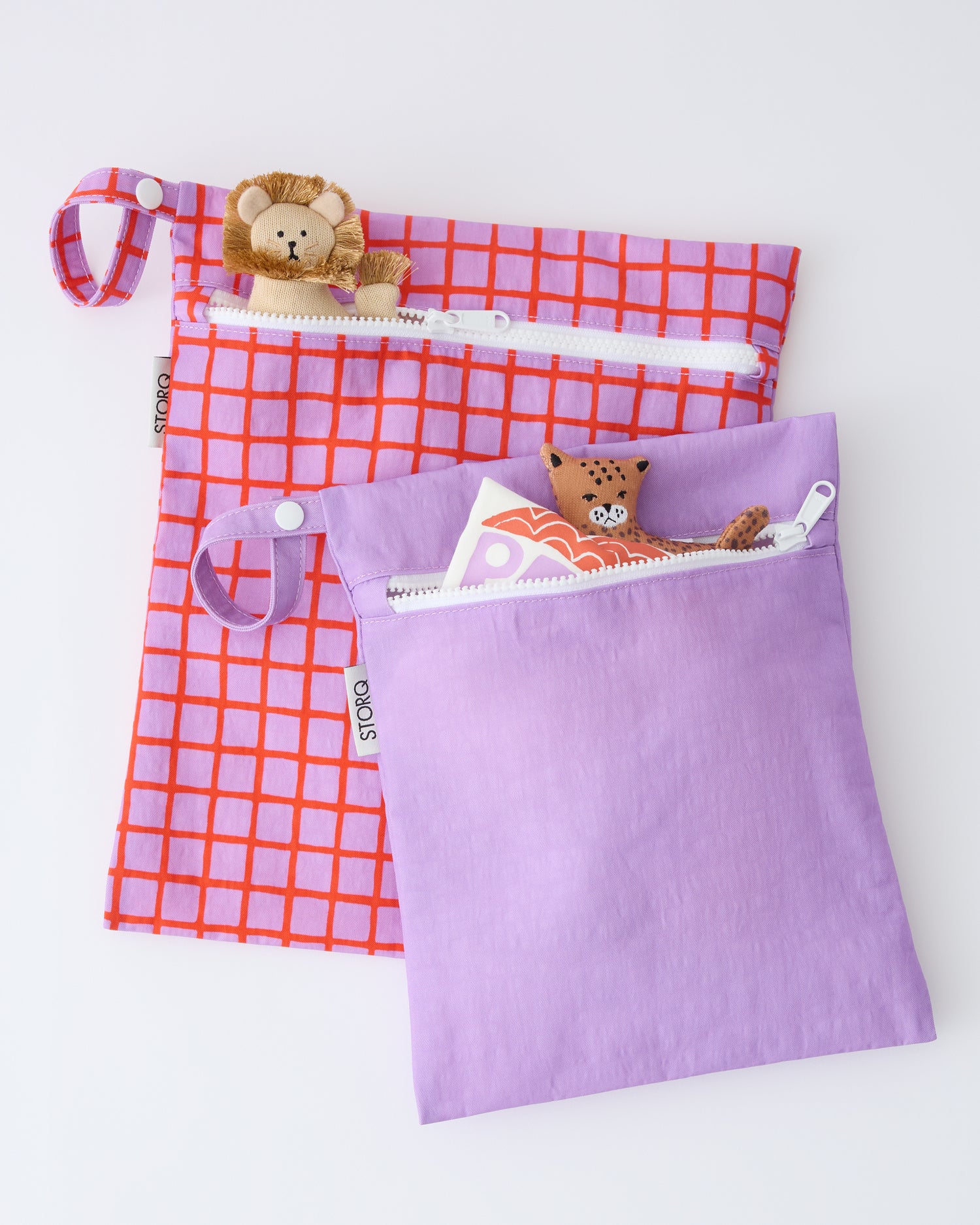 Wet/Dry Bag Set in Orchid Grid with toys sticking out of both, on a beige background.