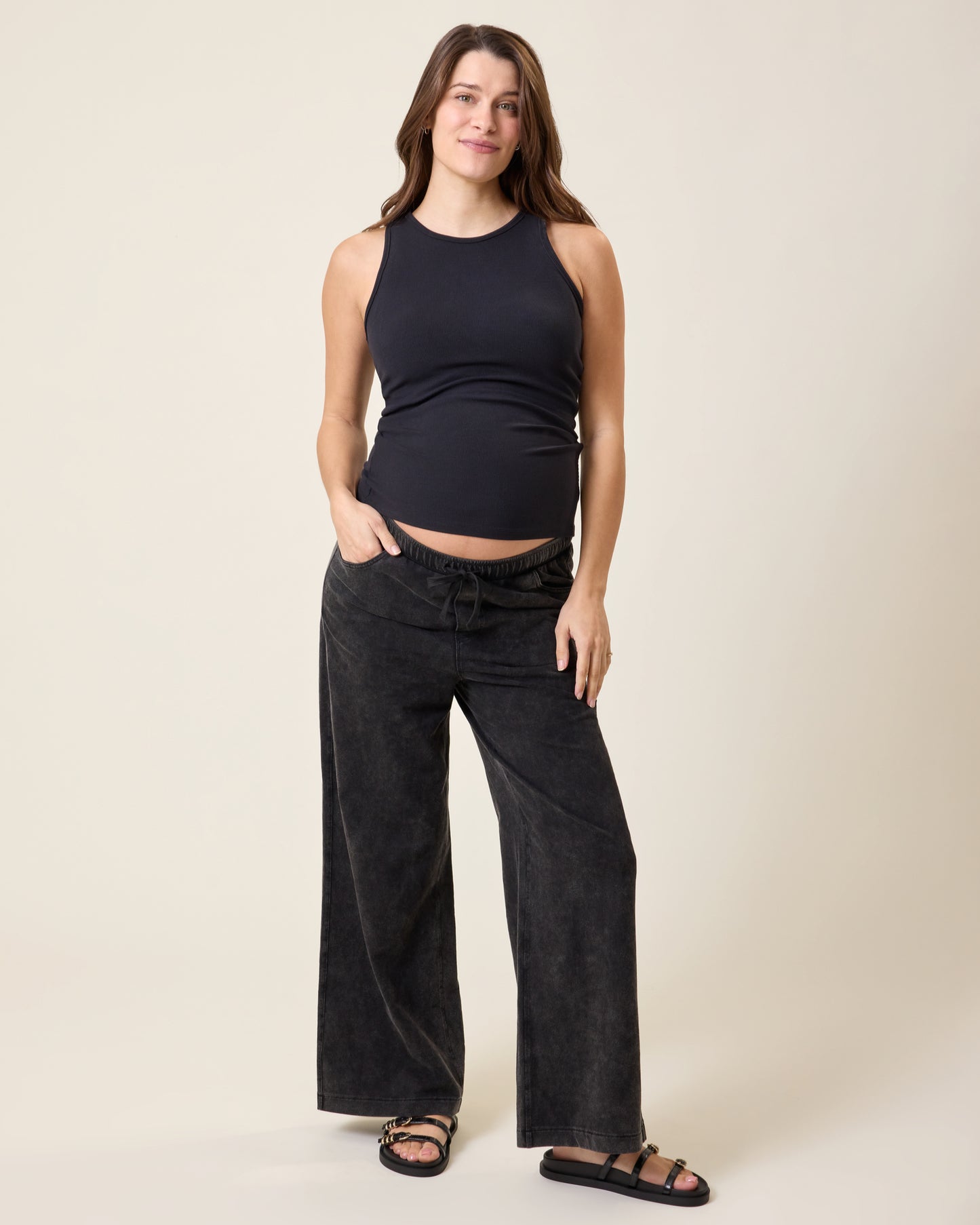 Woman wearing the Ribbed Bamboo Racerback Nursing Tank in black and Wide Leg Maternity & Postpartum Drawstring Pant in dark wash on a beige background