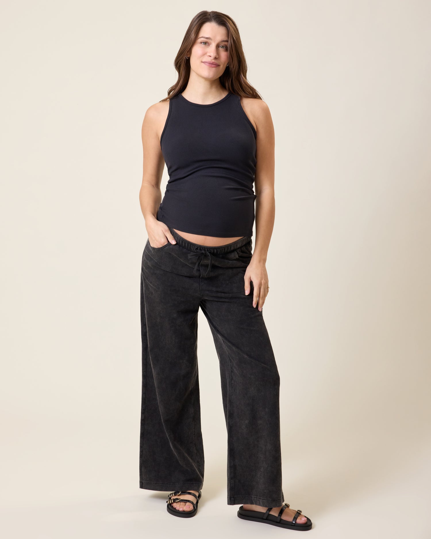 Woman wearing the Ribbed Bamboo Racerback Nursing Tank in black and Wide Leg Maternity & Postpartum Drawstring Pant in dark wash on a beige background
