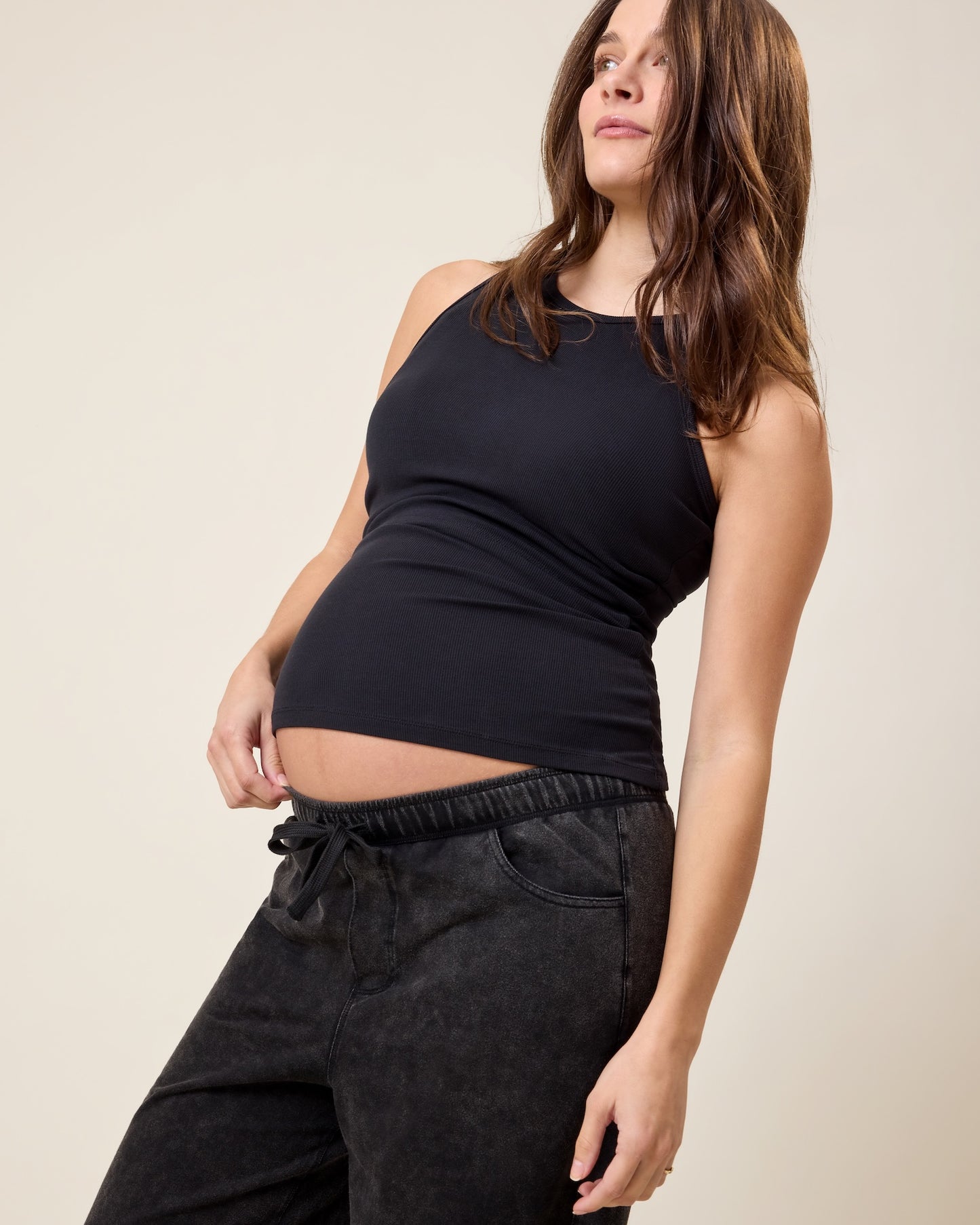 Woman wearing the Ribbed Bamboo Racerback Nursing Tank in black and Wide Leg Maternity & Postpartum Drawstring Pant in dark wash on a beige background