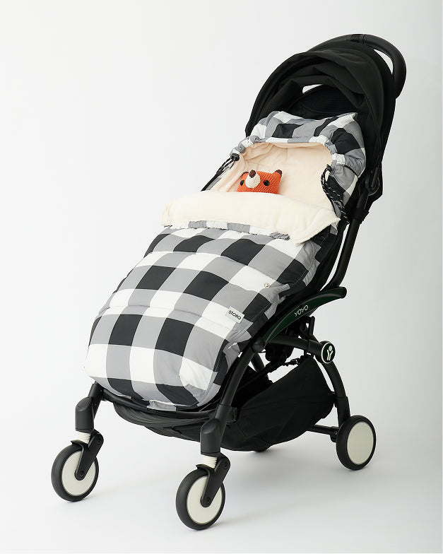 Cozy Stroller Footmuff in Buffalo Plaid in a black stroller with fox lovey snuggled in and peeking out, on an off white background.