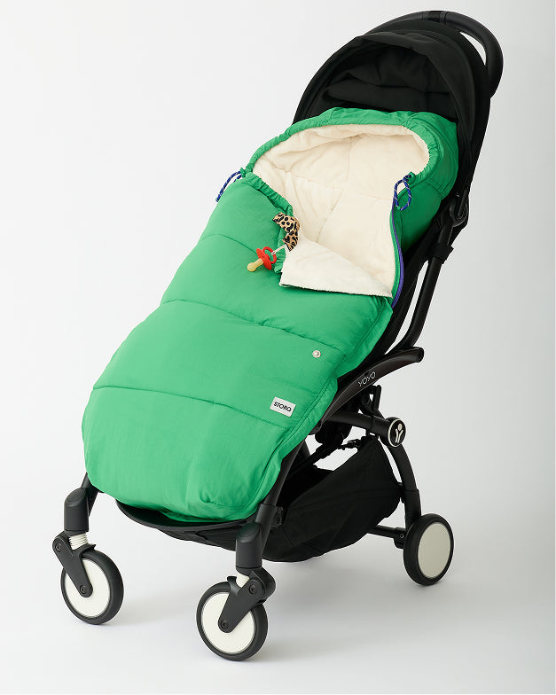 Cozy Stroller Footmuff in Green secured into a black stroller with Leopard pacifier clip attached and corner pulled down to show fuzzy interior, on an off white background.