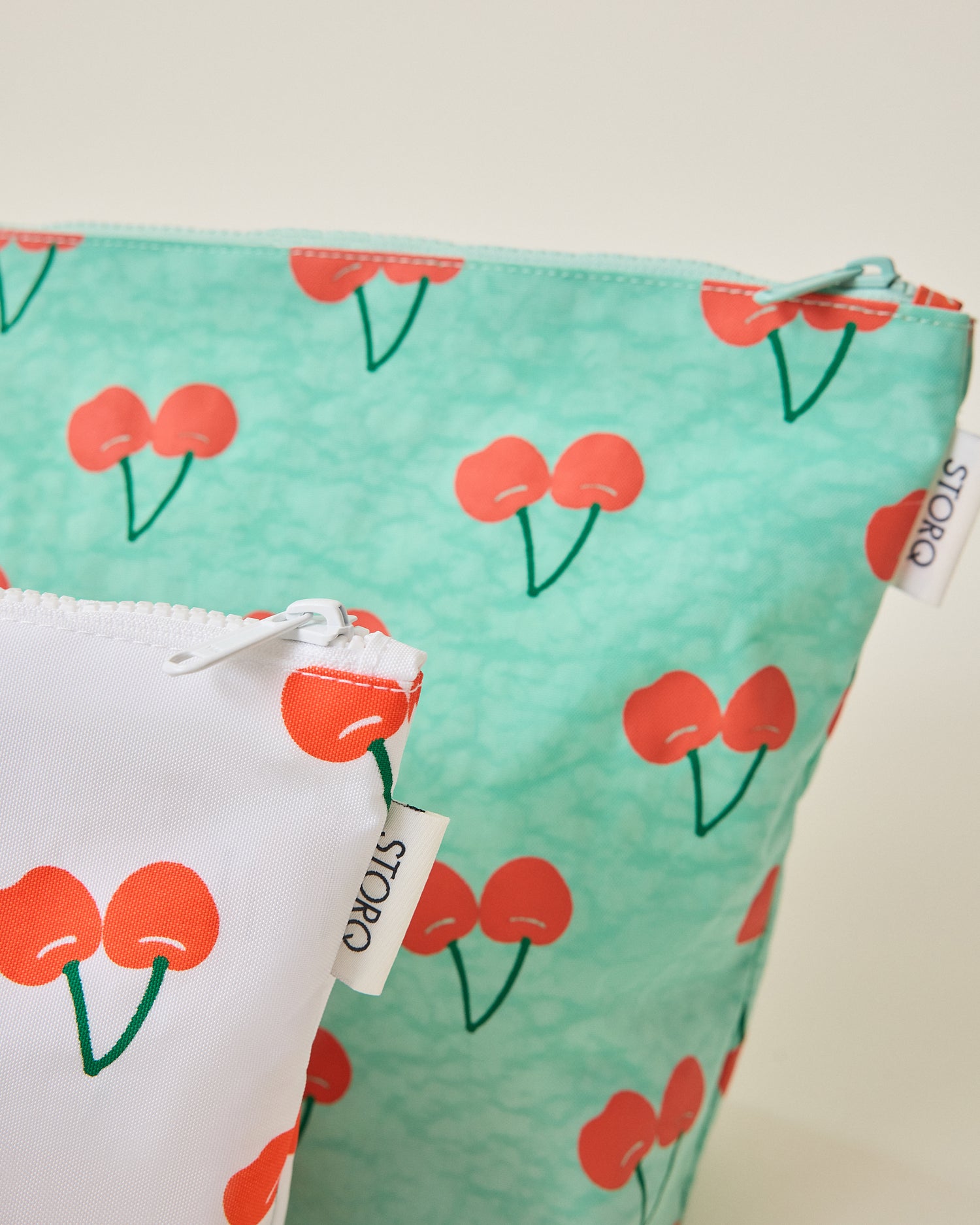 Close up of green and white pouches of the Zipper Pouch Three-Piece Set in Cherries print on a beige background