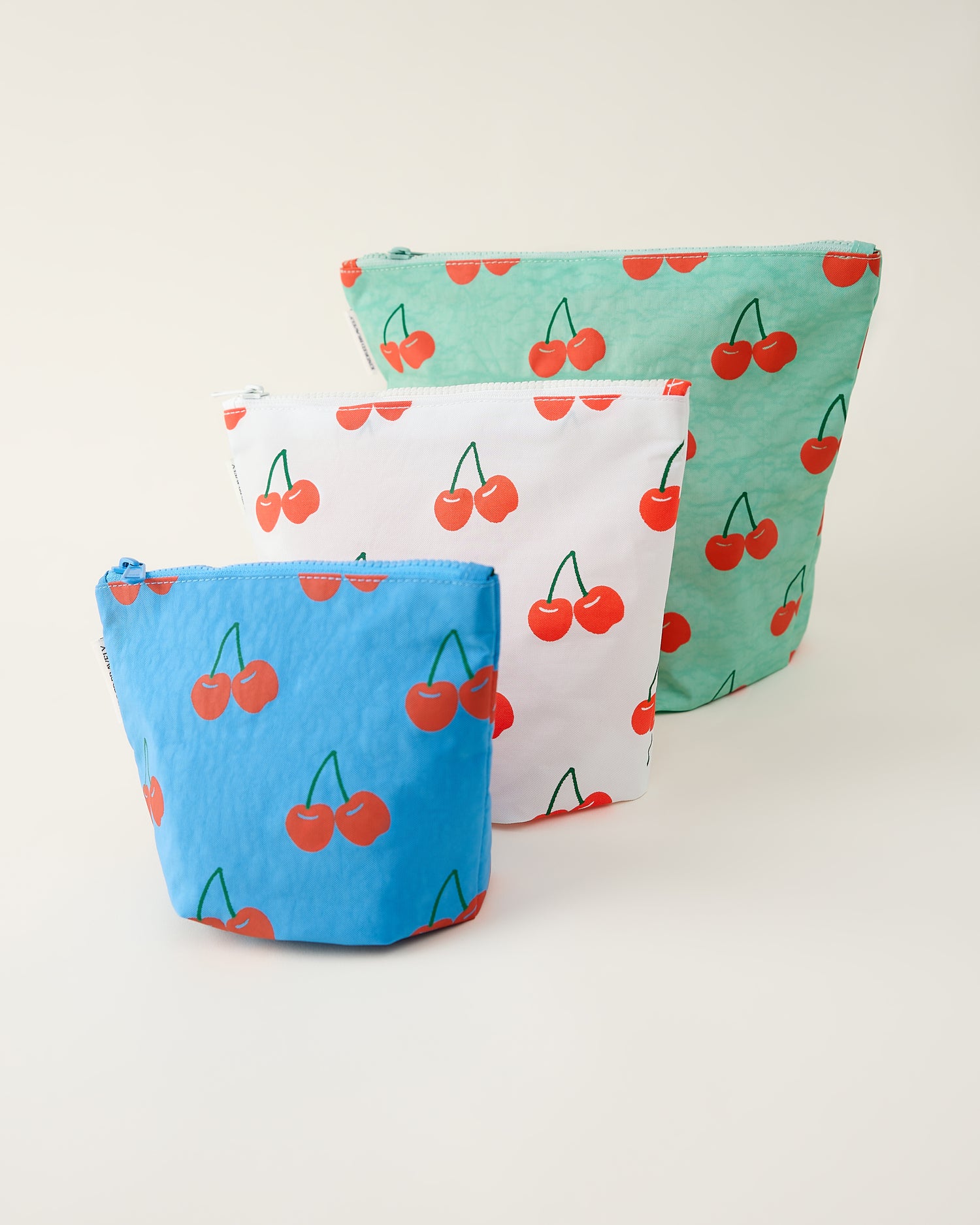 Three zipper pouches with cherry pattern on a beige background