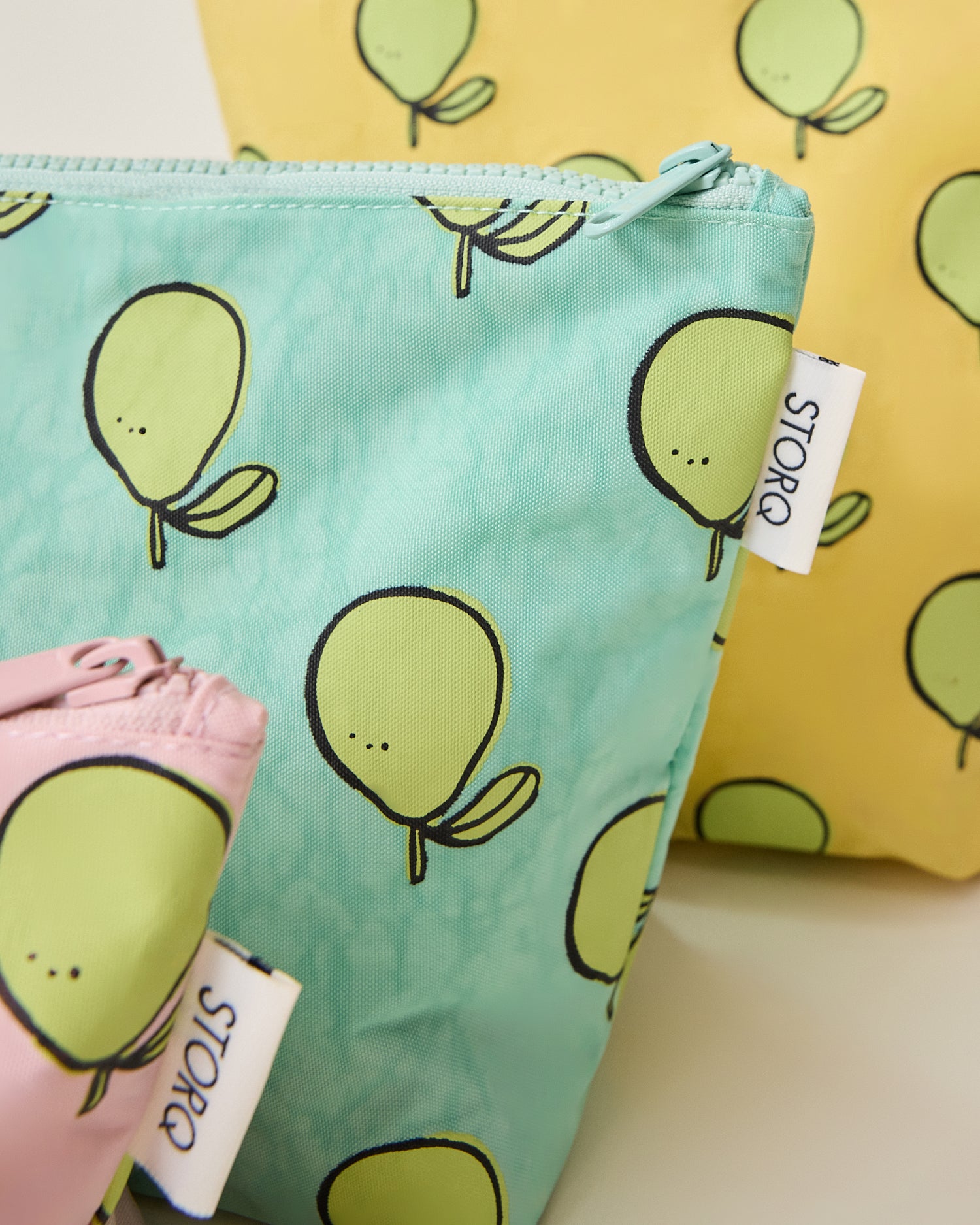 Close up of the yellow, green and pink pouches of the Zipper Pouch Three-Piece Set in Pomelo print on a beige background