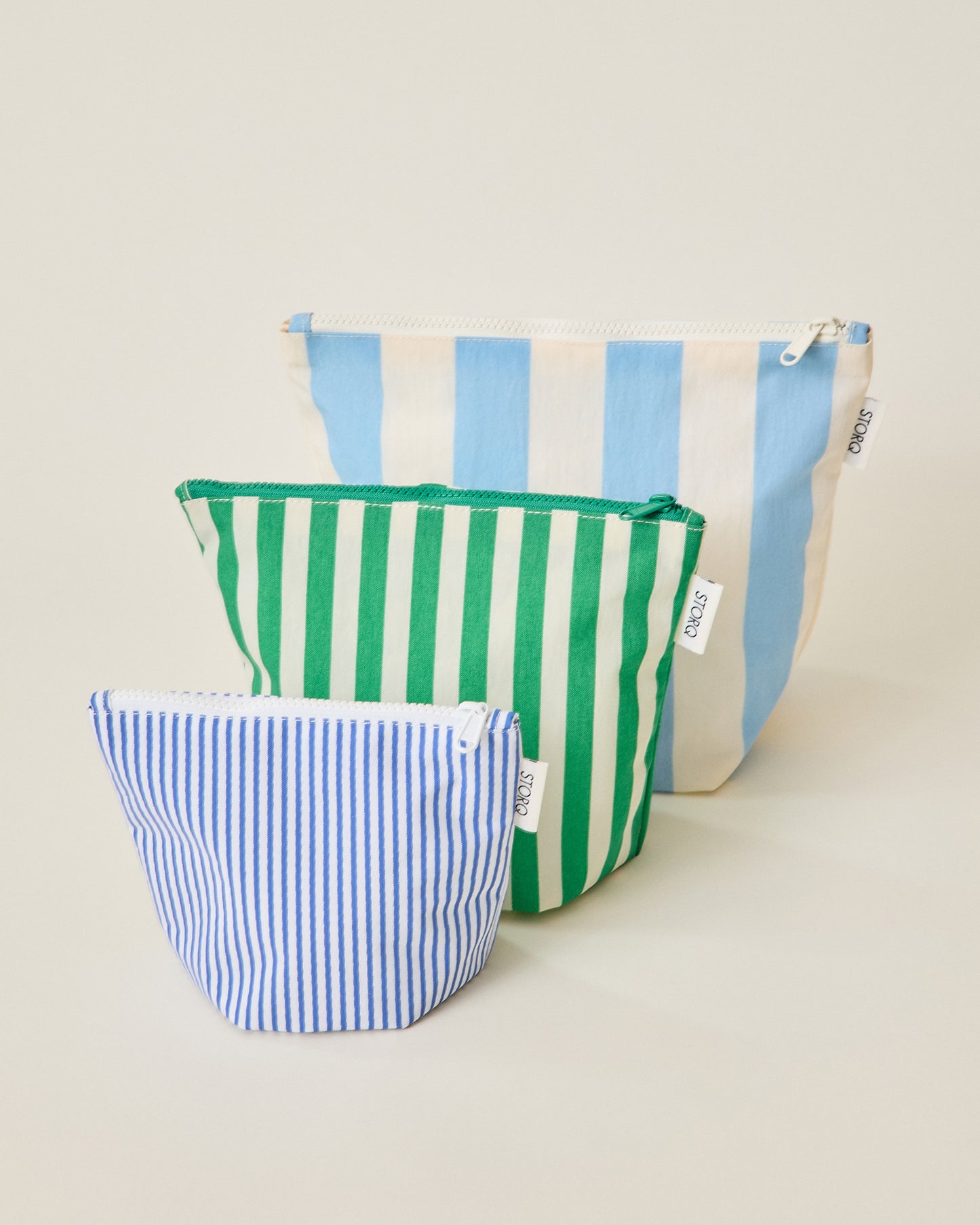 The wide blue stripe, wide green stripe and thin blue stripe pouches of the Zipper Pouch Three-Piece Set in Stripe print on a beige background
