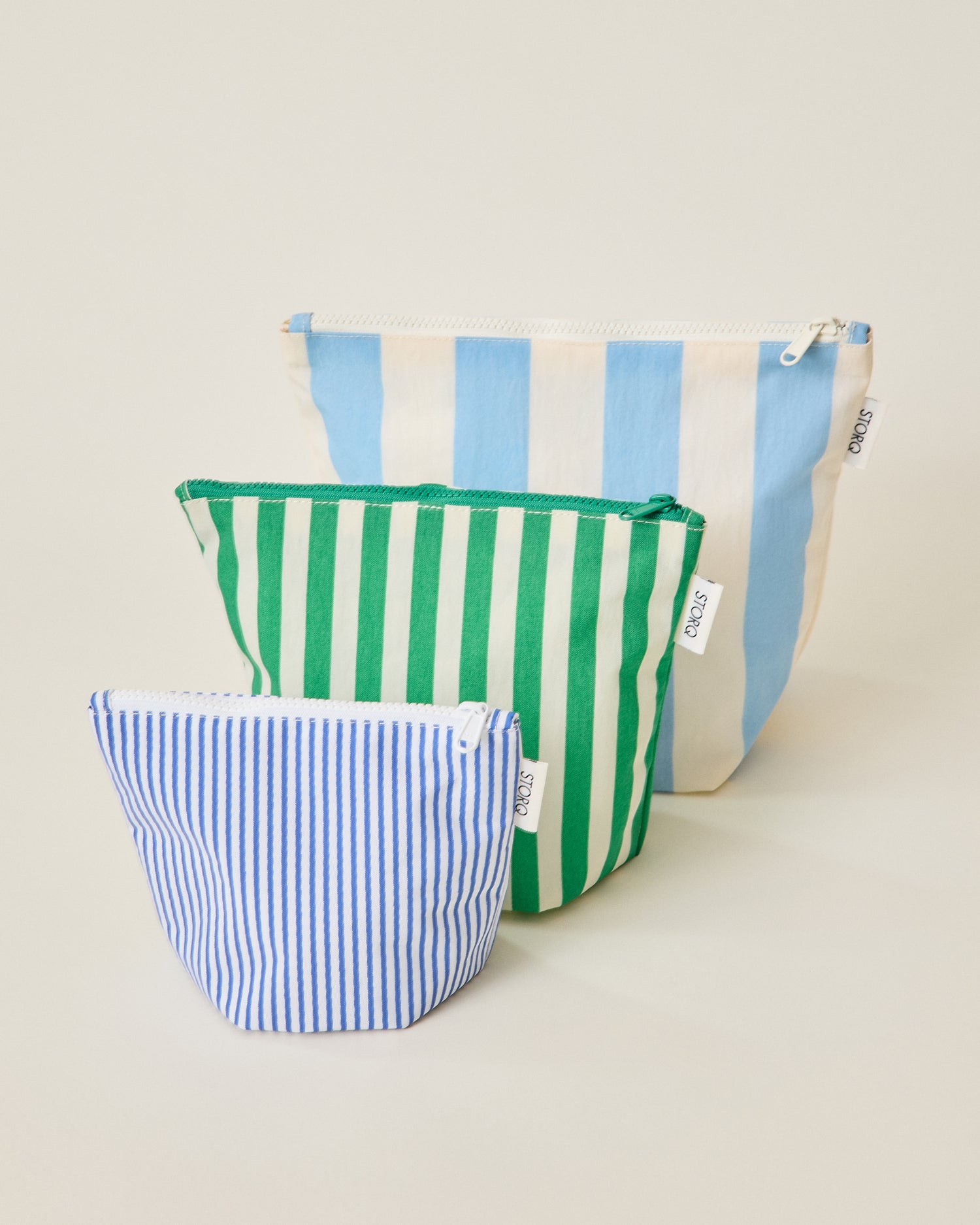 The wide blue stripe, wide green stripe and thin blue stripe pouches of the Zipper Pouch Three-Piece Set in Stripe print on a beige background