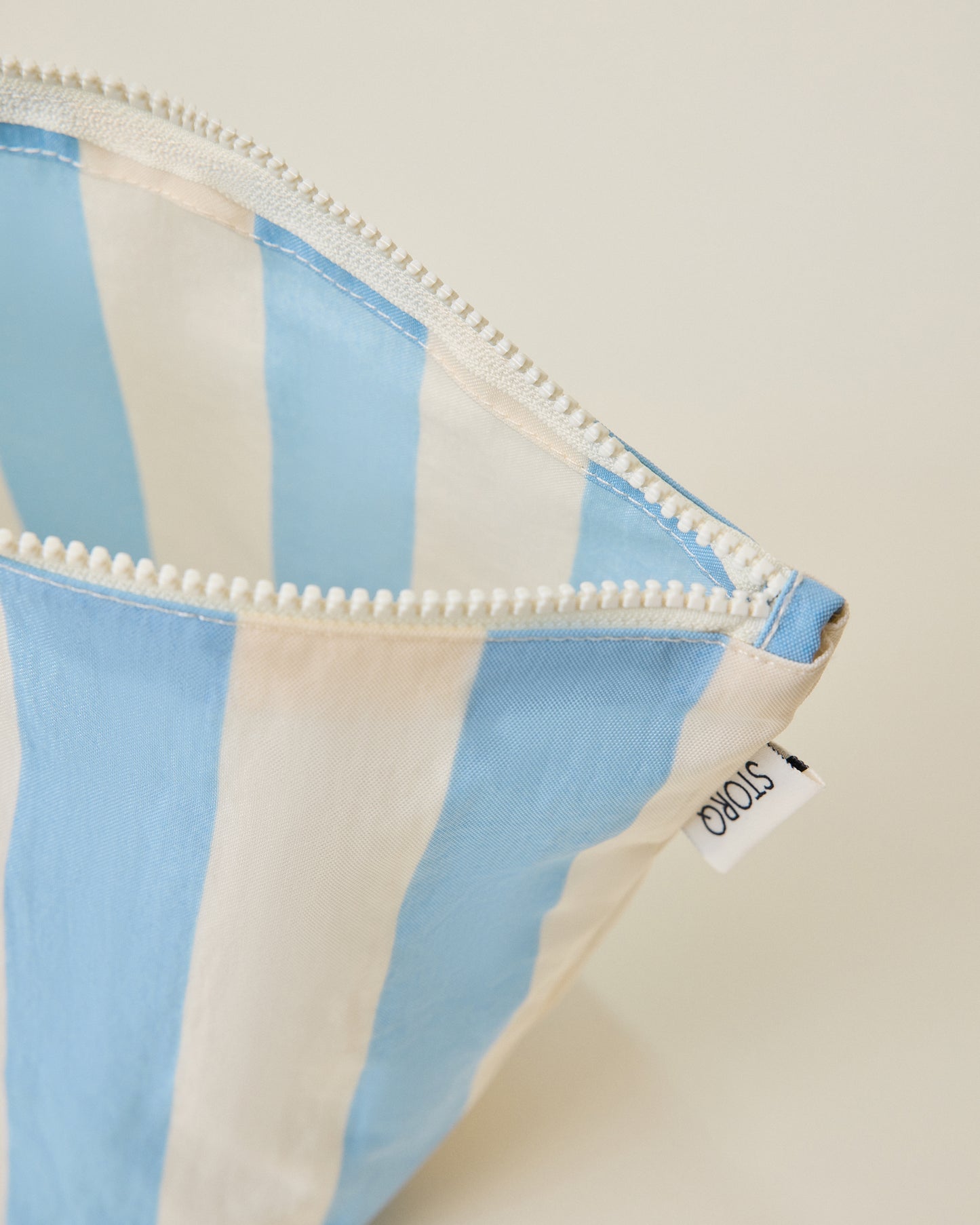 Close up of the wide blue stripe pouch of the Zipper Pouch Three-Piece Set in Stripe print on a beige background