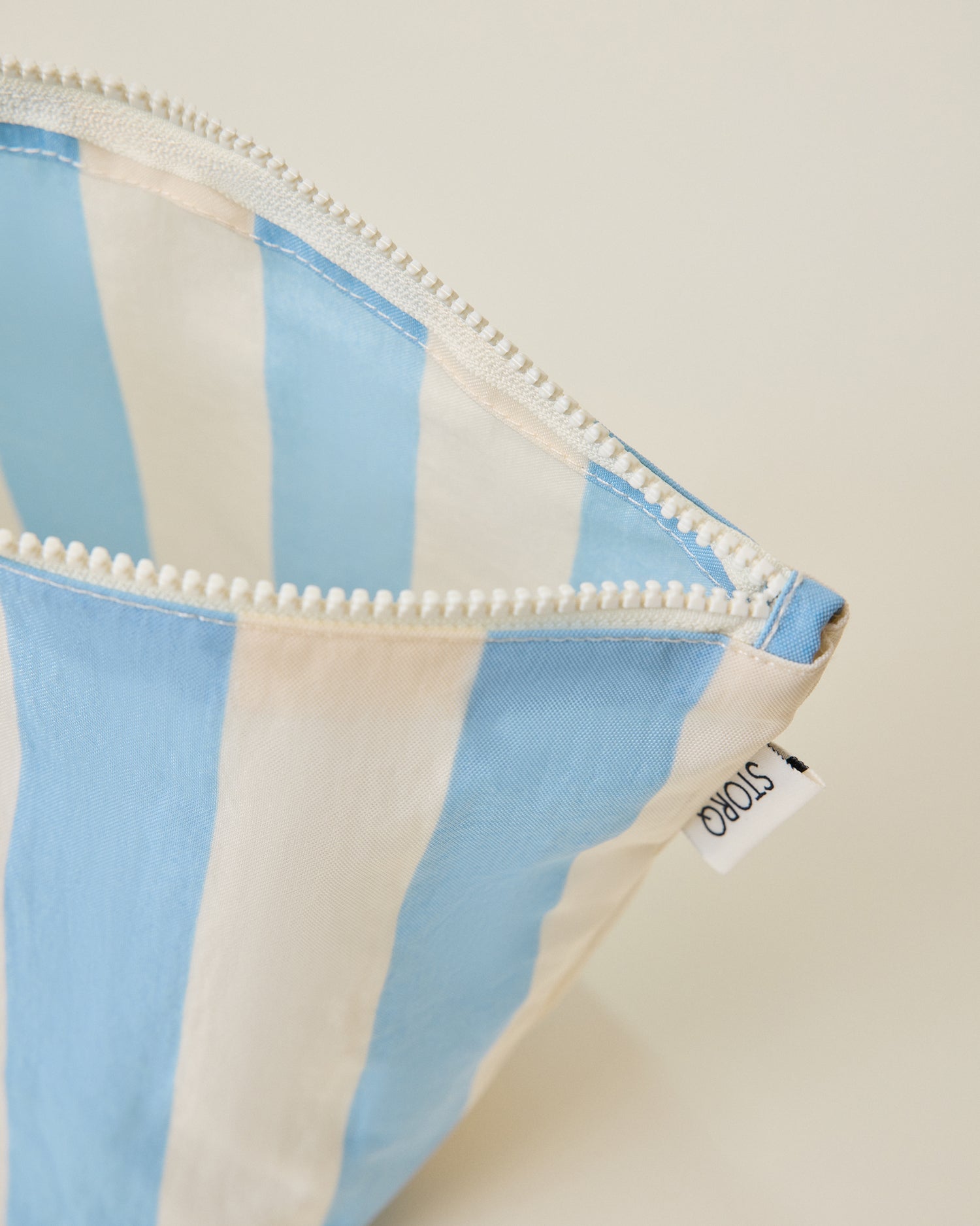 Close up of the wide blue stripe pouch of the Zipper Pouch Three-Piece Set in Stripe print on a beige background