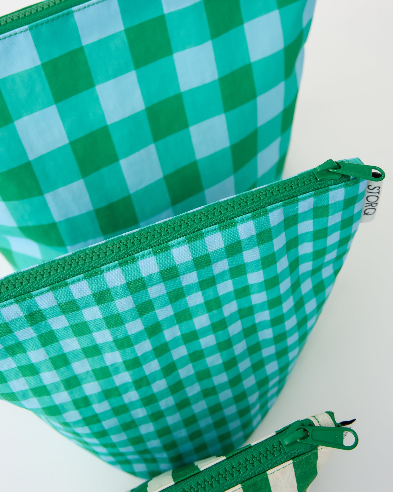 Close up on the zippers of the Zipper Pouch Three-Piece Set in Teal Gingham on a beige background.