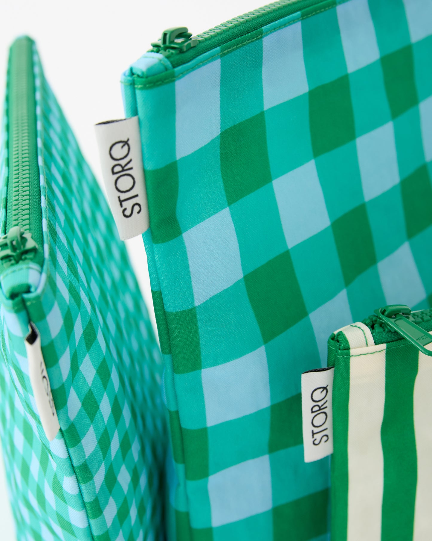 Close up of the various patterns of the Zipper Pouch Three-Piece Set in Teal Gingham on a beige background.