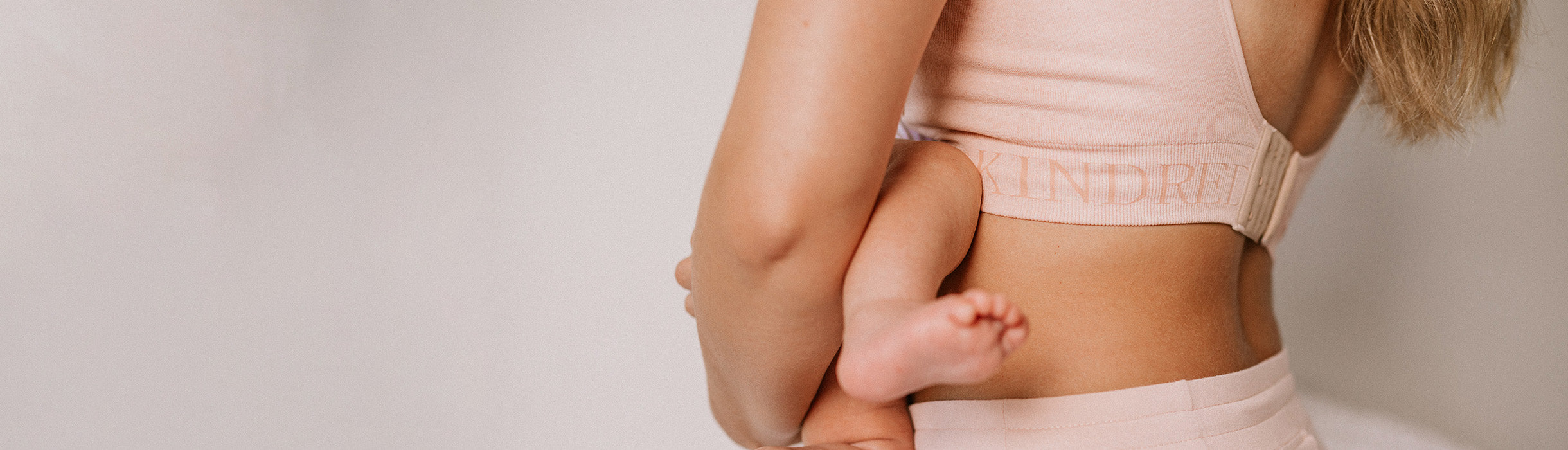 Cropped in image of model holding infant, showing Kindred Bravely bra band