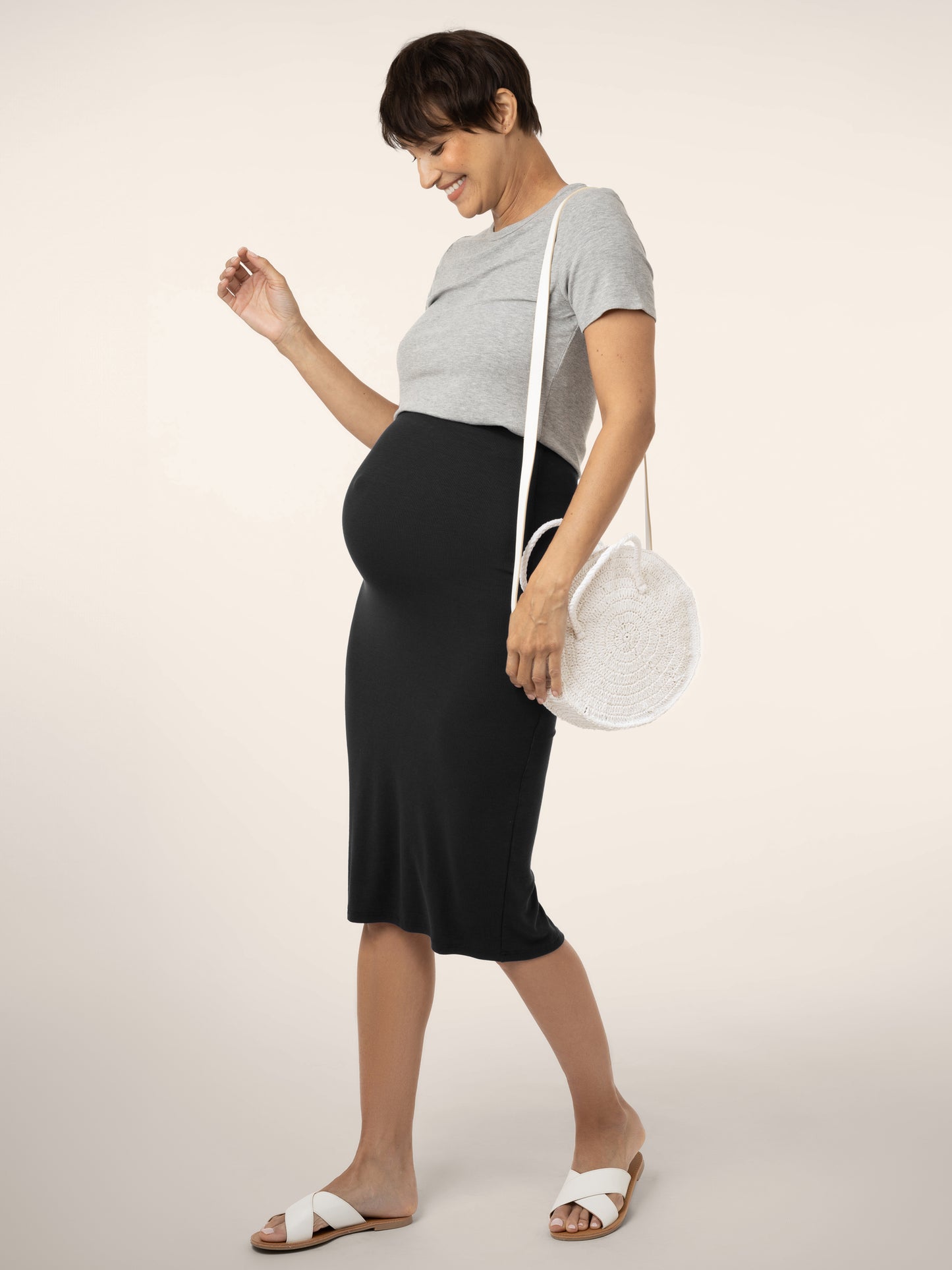 Full view of pregnant model wearing the Ribbed  Bamboo Maternity & Postpartum Midi Skirt in black, paired with t-shirt and sandals @model_info:Briana is 7 months pregnant and wearing a Small.
