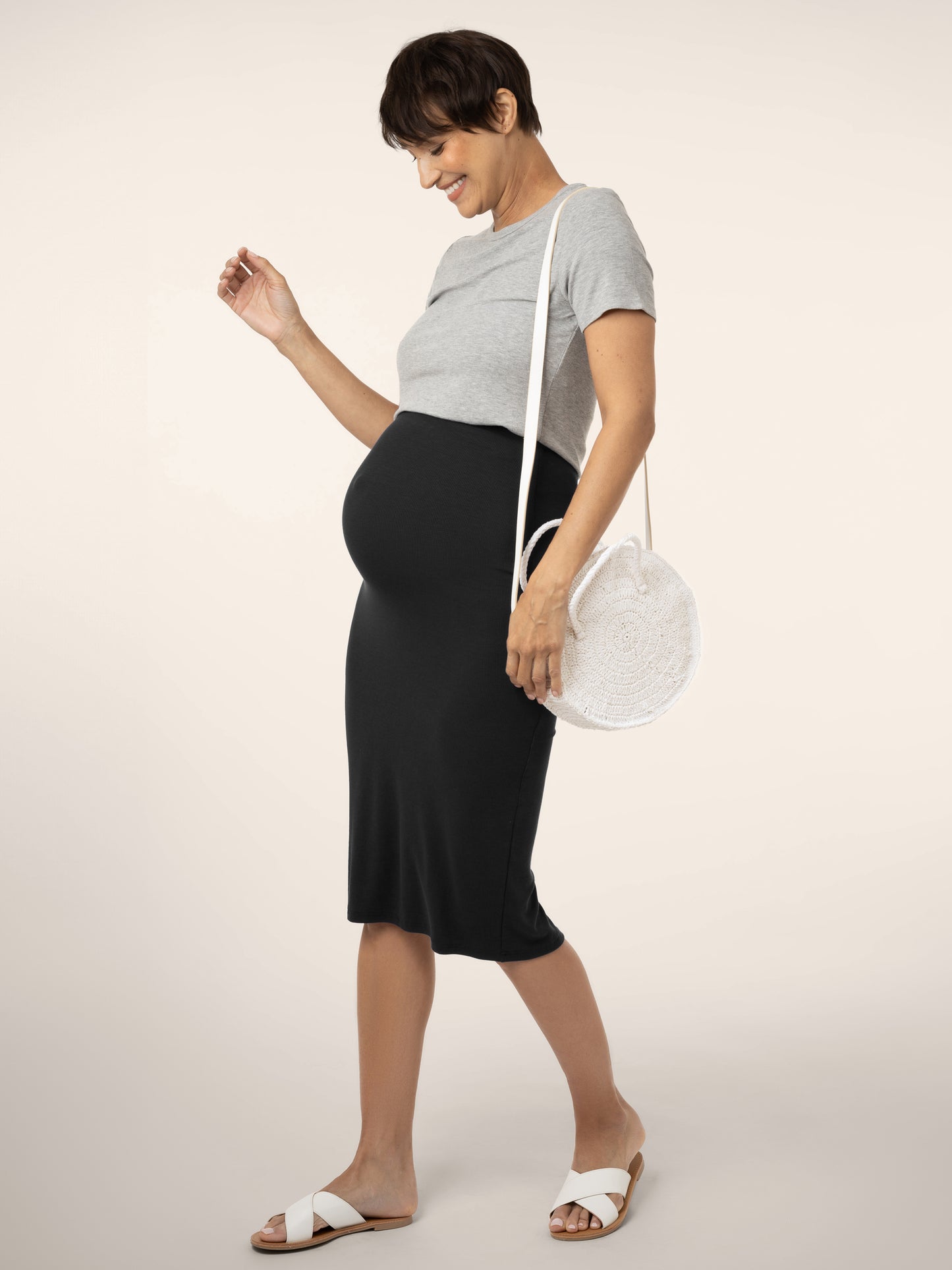 Full view of pregnant model wearing the Ribbed  Bamboo Maternity & Postpartum Midi Skirt in black, paired with t-shirt and sandals