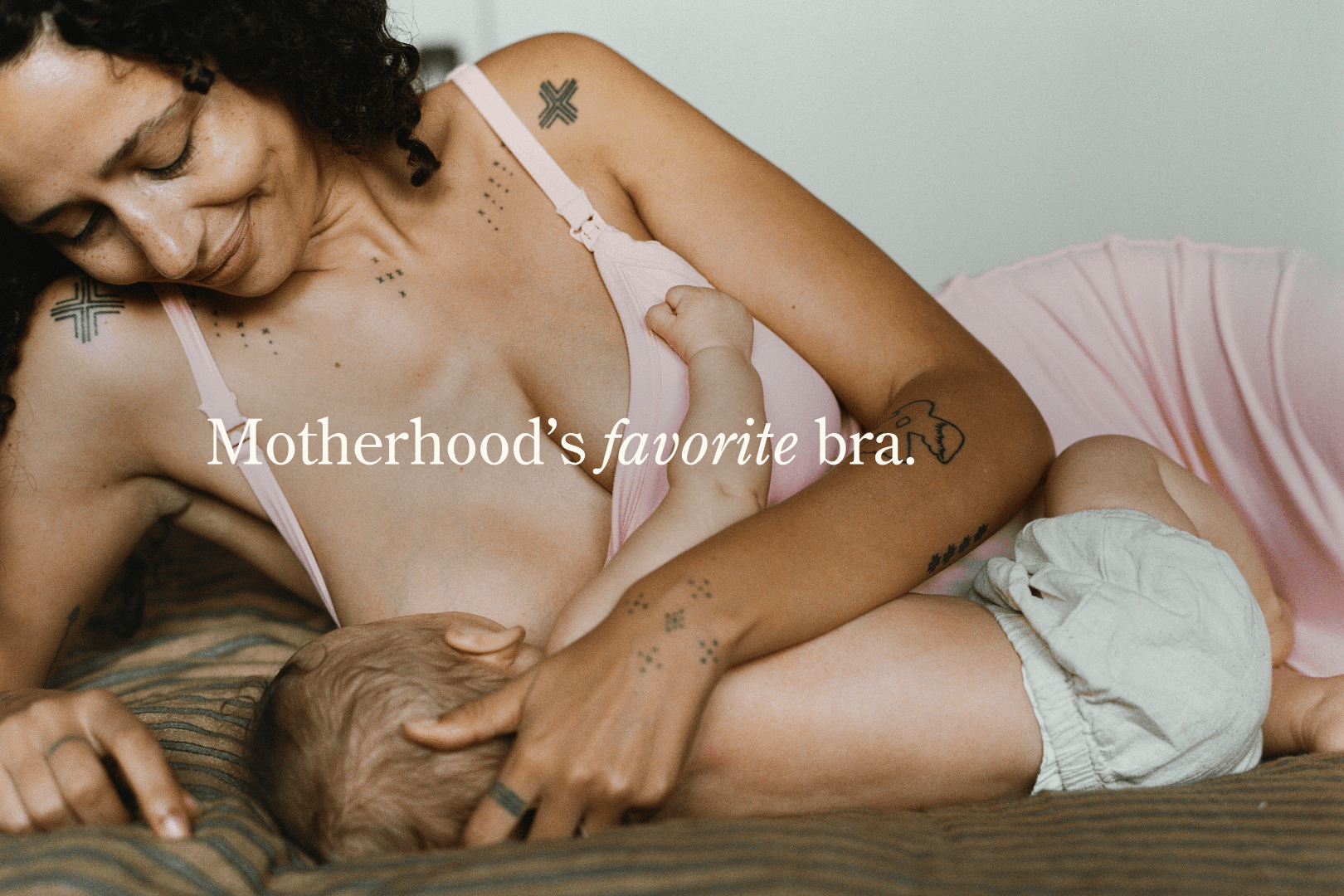 Rotating gif, white text stating Motherhood's favorite bra - pajamas - loungewear. Image of woman breastfeeding baby on bed while wearing The Sunday Maternity & Nursing Lounge Dress in Sunset Pink with beige background.