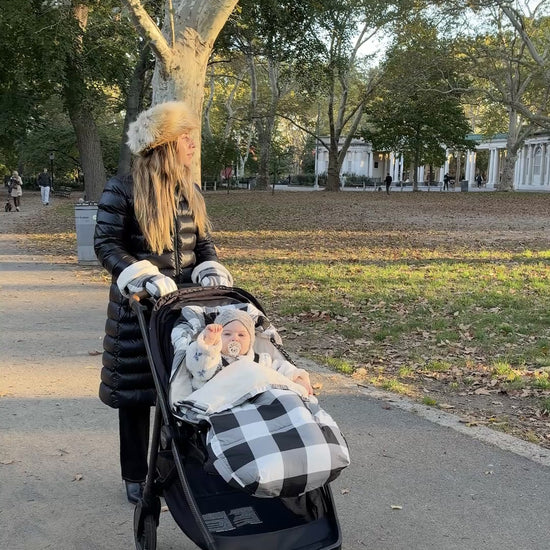 With mother and baby comforted by the The Bundle Up Stroller Set in Buffalo Plaid, they're both sure to enjoy their winter park excursion in comfort. Baby is waving with a little pacifier, fuzzy coat and woven hat. 