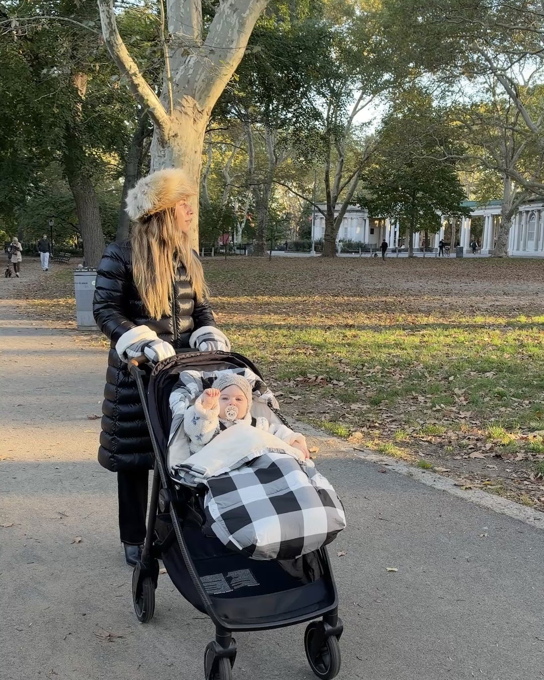 With mother and baby comforted by the The Bundle Up Stroller Set in Buffalo Plaid, they're both sure to enjoy their winter park excursion in comfort. Baby is waving with a little pacifier, fuzzy coat and woven hat. 