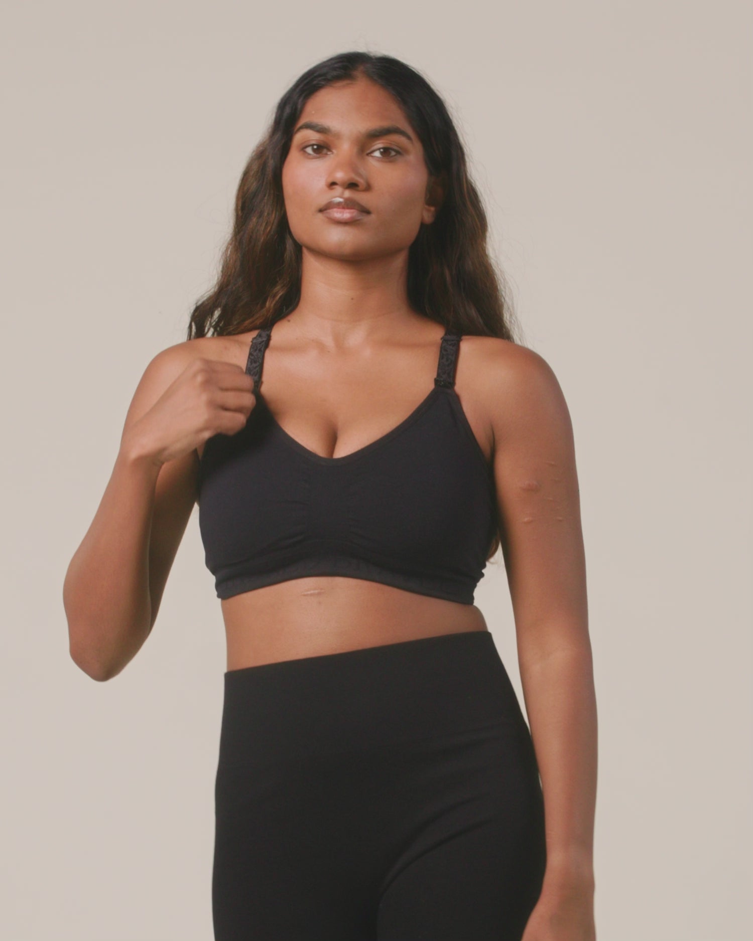 Video of model displaying comfort and function of the Sublime Hands-Free Pumping & Nursing Sports Bra in Black on a beige background. 