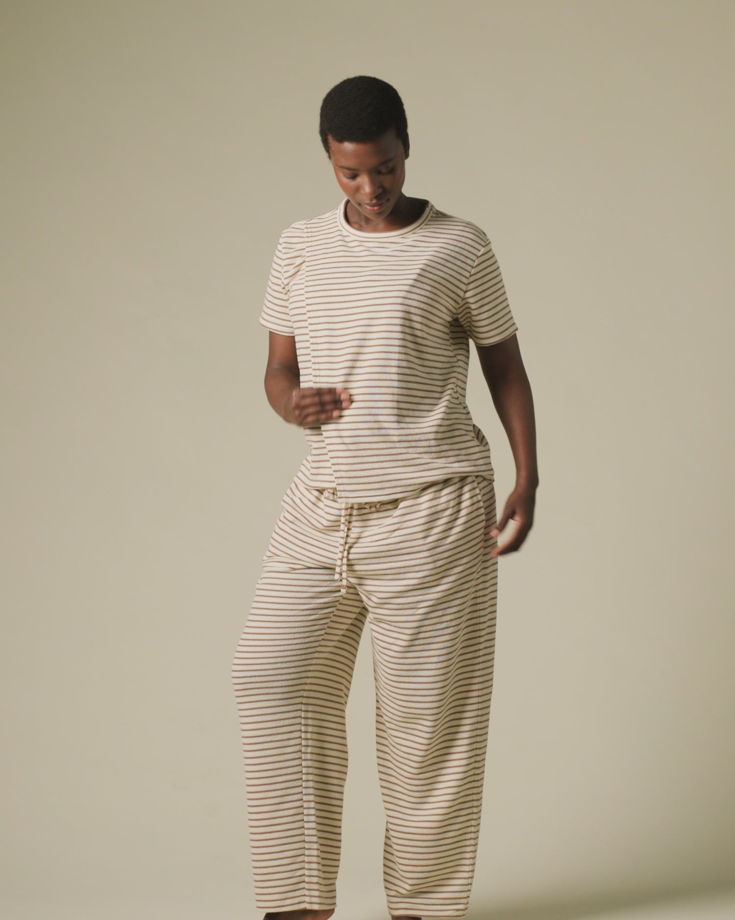 Video of model wearing Luxe Terry Maternity & Nursing Split Hem T-shirt in Ivory & Chocolate Stripe and Luxe Terry Maternity & Postpartum Pant in Ivory & Chocolate Stripe, on a beige background.