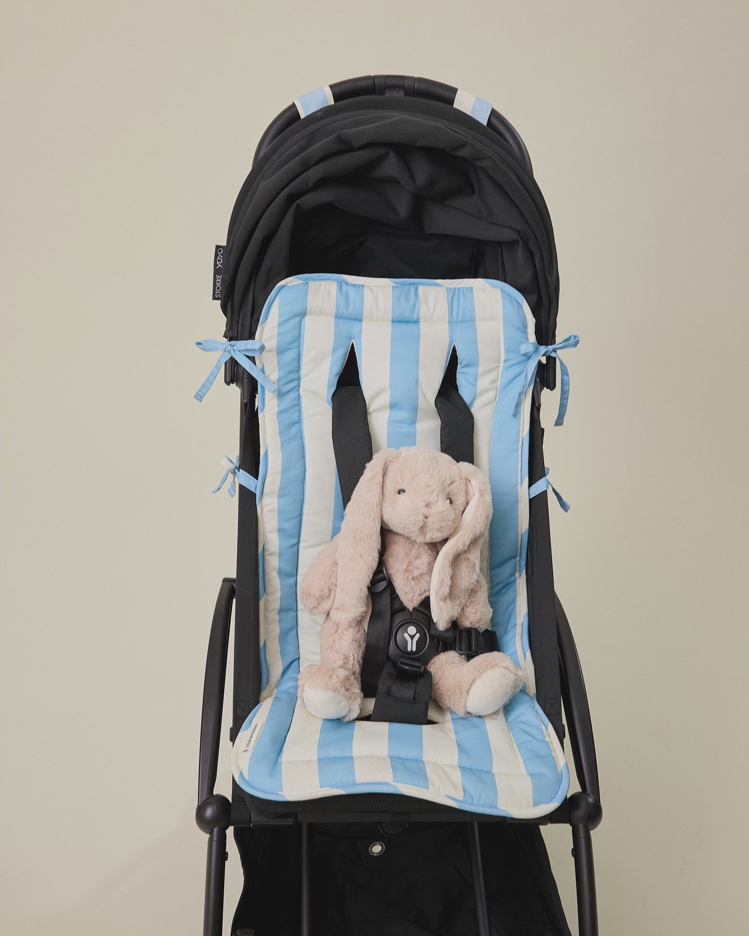 Video for the Stroller Party Set with Seat Liner, Party Clips and Caddy Bag in Blue Wide Stripe with small bunny doll buckled into stroller, on a beige background