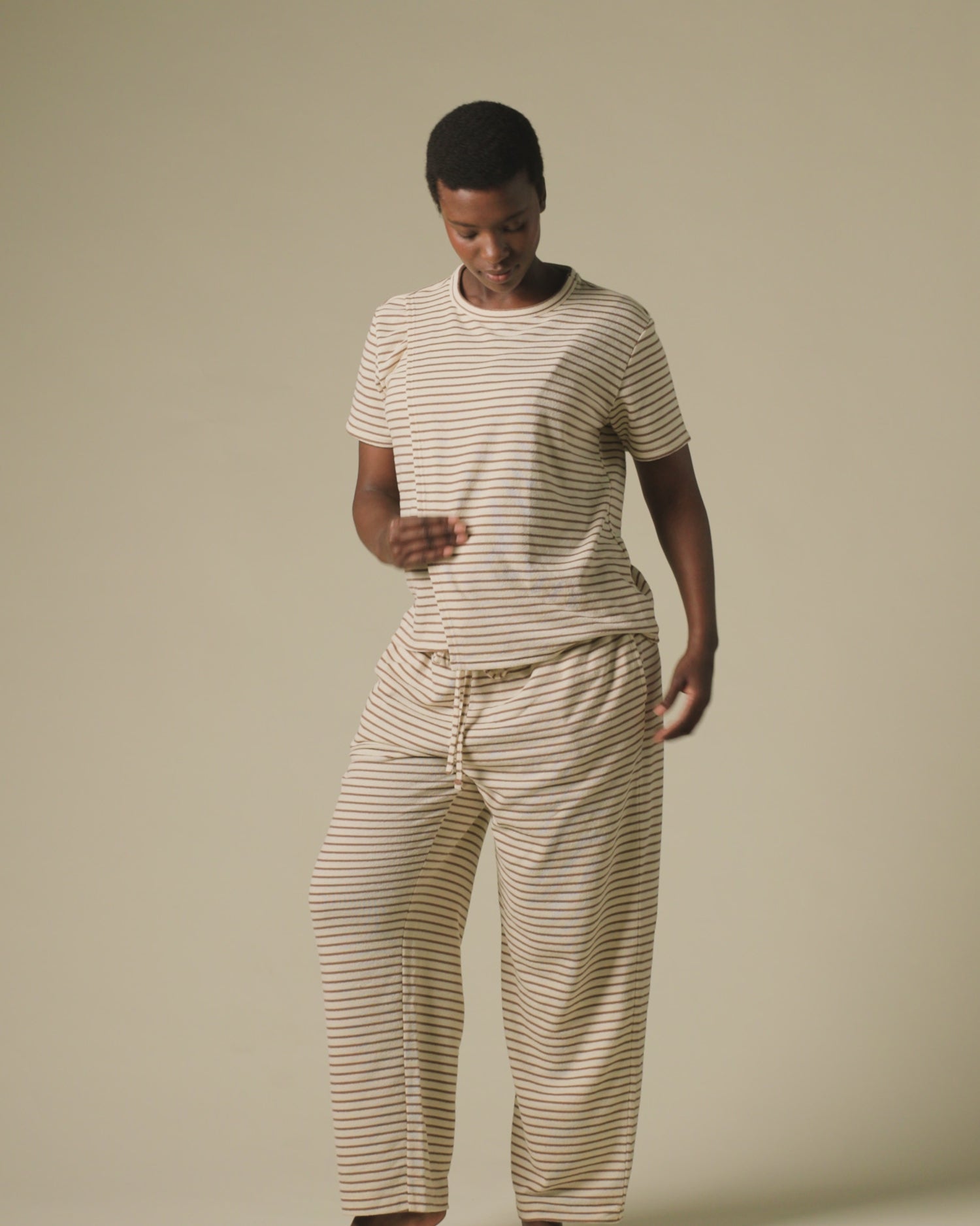 Video of model wearing Luxe Terry Maternity & Nursing Split Hem T-shirt in Ivory & Chocolate Stripe and Luxe Terry Maternity & Postpartum Pant in Ivory & Chocolate Stripe, on a beige background.