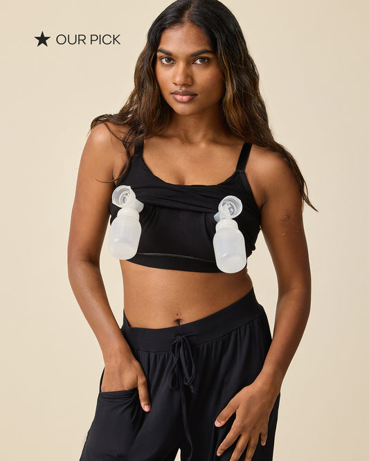 Black star and black text that reads: OUR PICK. Model is wearing Sublime Hands-Free Pumping & Nursing Sleep and Lounge Bra in Black. She pulled up the pumping layer to insert pumps for hands-free pumping access. On a beige background.