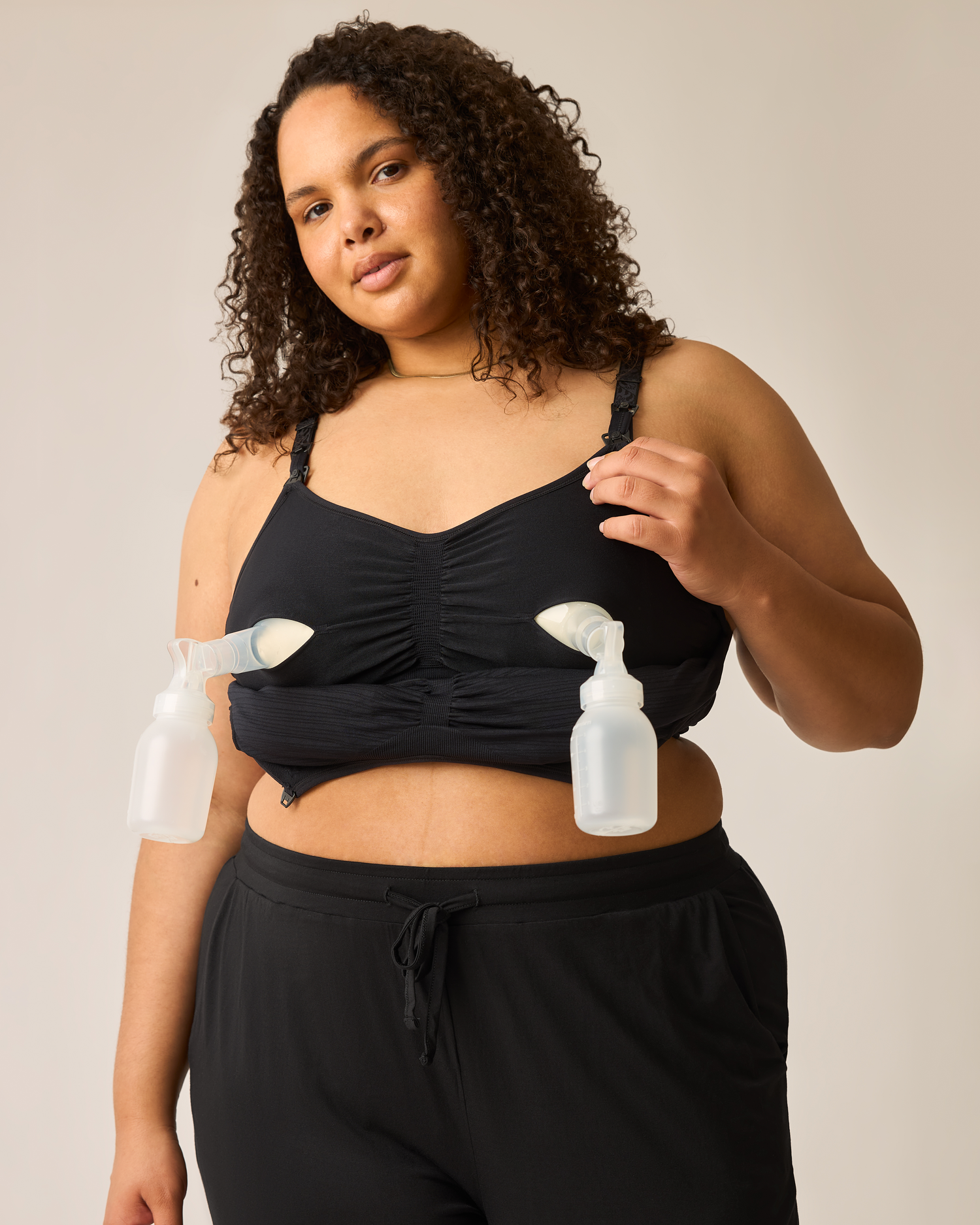 Woman wearing the Sublime® Hands-Free Pumping & Nursing Bra in black with two pump flanges inserted on plain background@model_info:Ionna is wearing a 1X Busty.